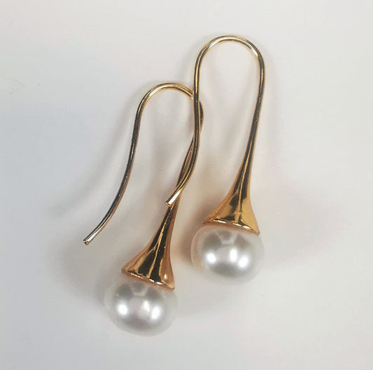 Boucles d'oreilles perles de culture blanches 9mm sur pendants longs plaqués or. Présentées cote o cote, perles en bas, pendants tournés vers la gauche, boucle droite décalée vers le haut, sur fond blanc. Vue de dessus.