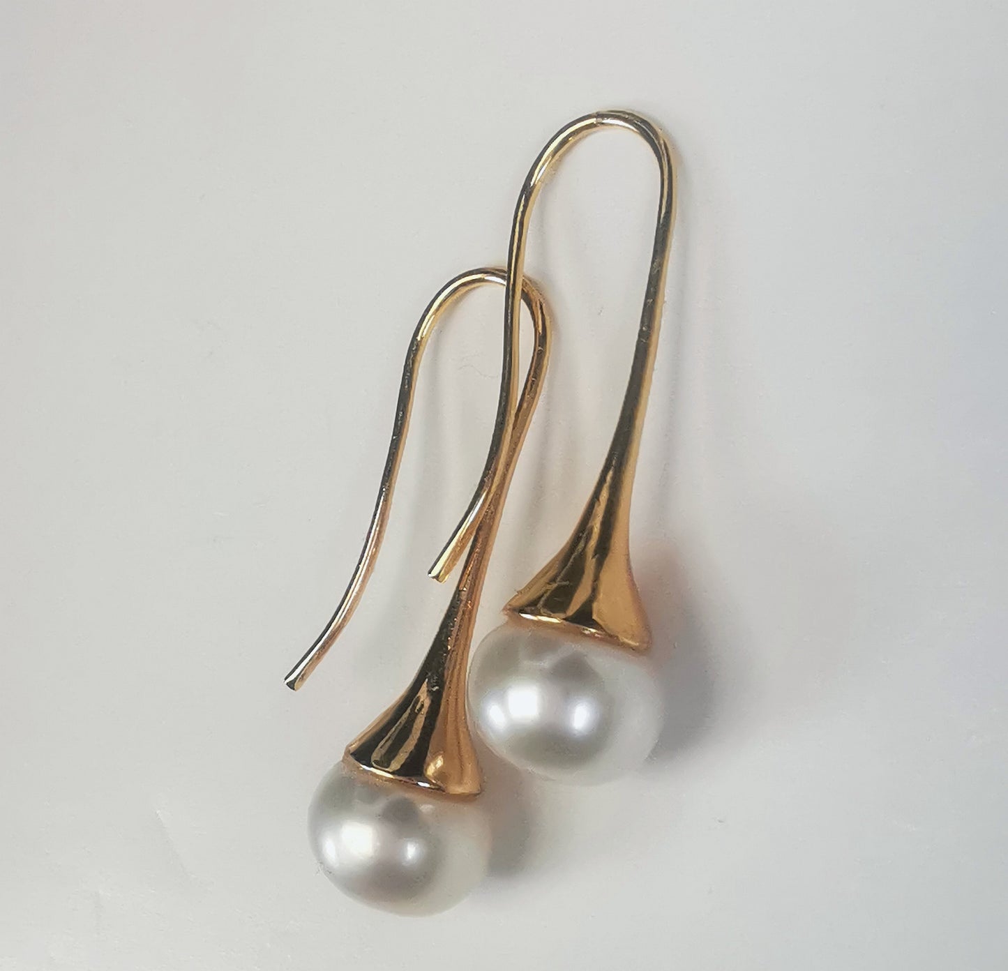 Boucles d'oreilles perles de culture blanches 9mm sur pendants longs plaqués or. Présentées cote o cote, perles en bas, pendants tournés vers la gauche, boucle droite décalée vers le haut, sur fond blanc. Vue de la droite.