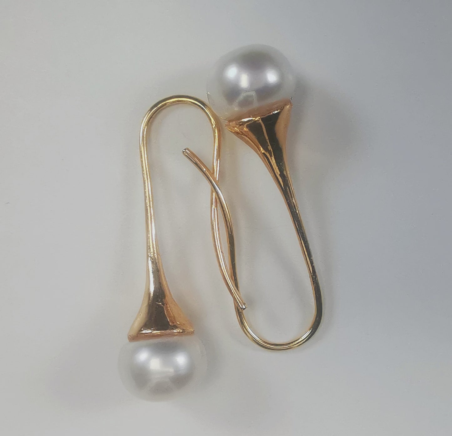 Boucles d'oreilles perles de culture blanches 9mm sur pendants longs plaqués or. Présentées cote o cote, boucle de gauche perle en bas, pendant tourné vers la droite, , celle de droite, perle en haut, pendant tourné vers la gauche, sur fond blanc. Vue de dessus.