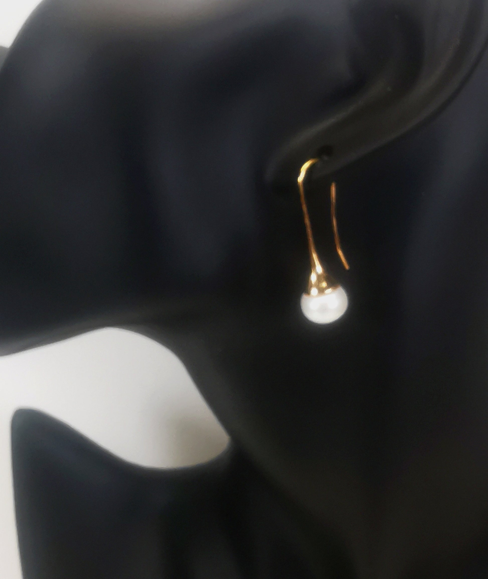 Boucles d'oreilles perles de culture blanches 9mm sur pendants longs plaqués or. représentées par une boucle accrochée à l'oreilles d'un mannequin buste noir. Vue de coté.