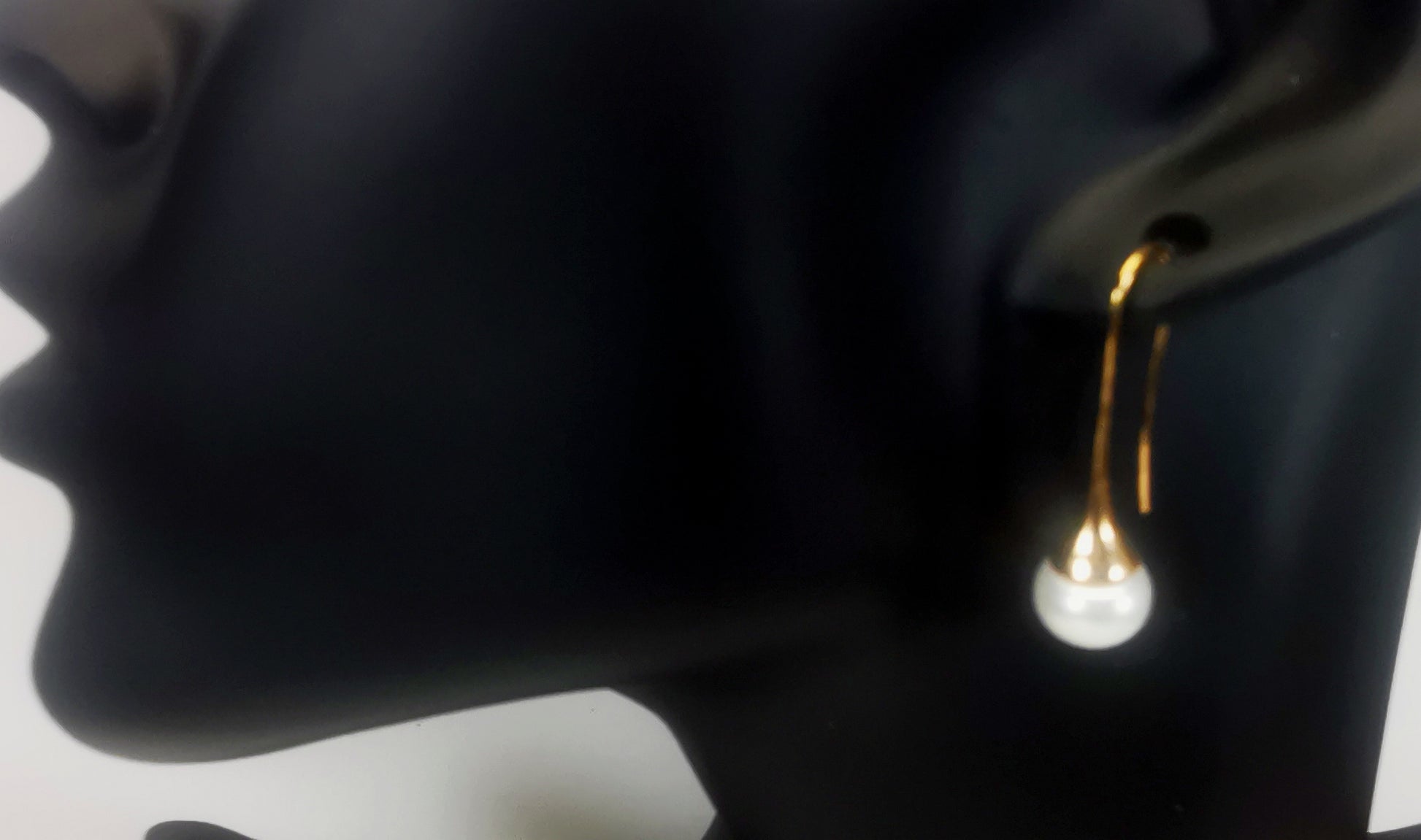Boucles d'oreilles perles de culture blanches 9mm sur pendants longs plaqués or. représentées par une boucle accrochée à l'oreilles d'un mannequin buste noir. Vue en gros plan de trois quarts face.