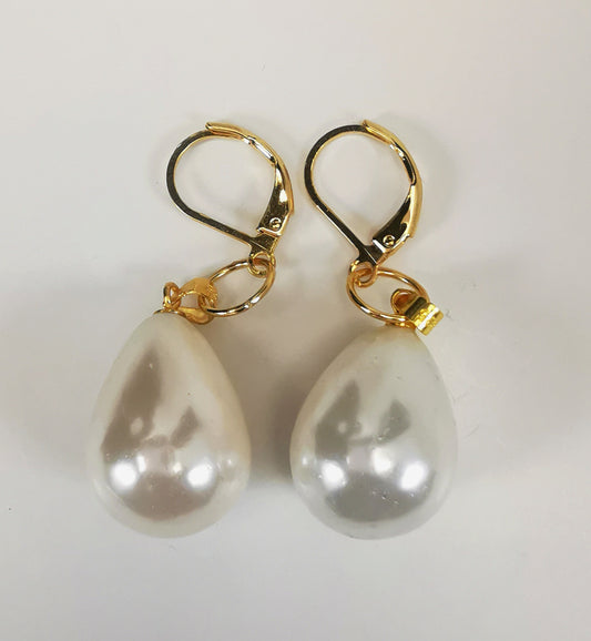 Boucles d'oreille en perles en forme de goutte d'eau blanches de 20x14mm taillées dans du coquillage avec émail artificiel. Les perles sont accrochées à une dormeuse via une bélière et un anneau, le tout plaqué or. Présentées cote à cote, perles en bas, sur fond blanc. Vue de dessus.