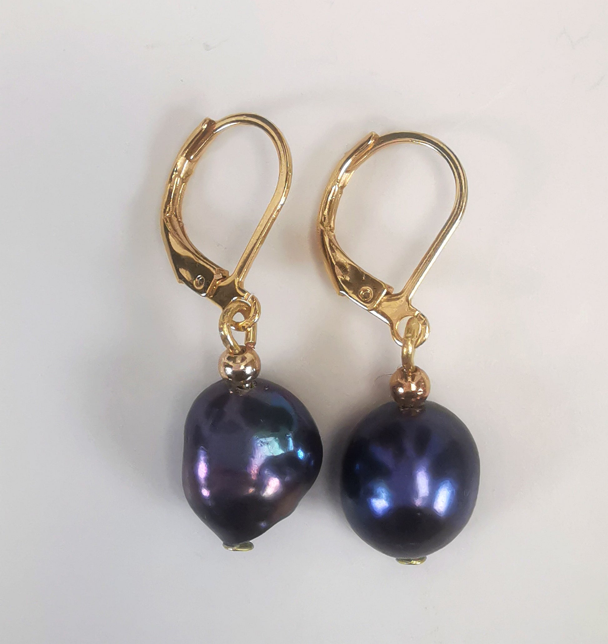 Boucles d'oreilles perles de culture noires baroques 10-12mm montées sur dormeuses plaquées or. Présentées cote à cote, perles en bas, sur un fond blanc. Vue de dessus.