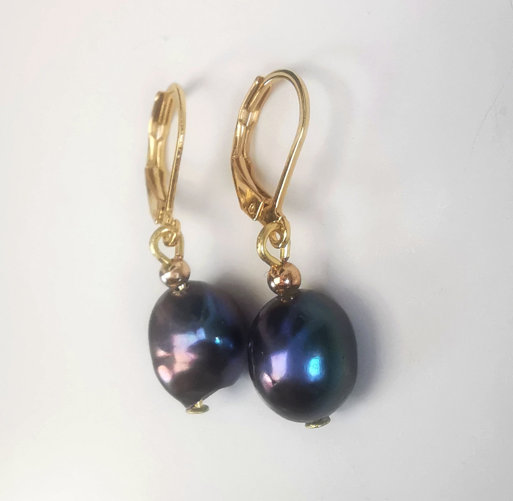 Boucles d'oreilles perles de culture noires baroques 10-12mm montées sur dormeuses plaquées or. Présentées cote à cote, perles en bas, sur un fond blanc. Vue de droite.