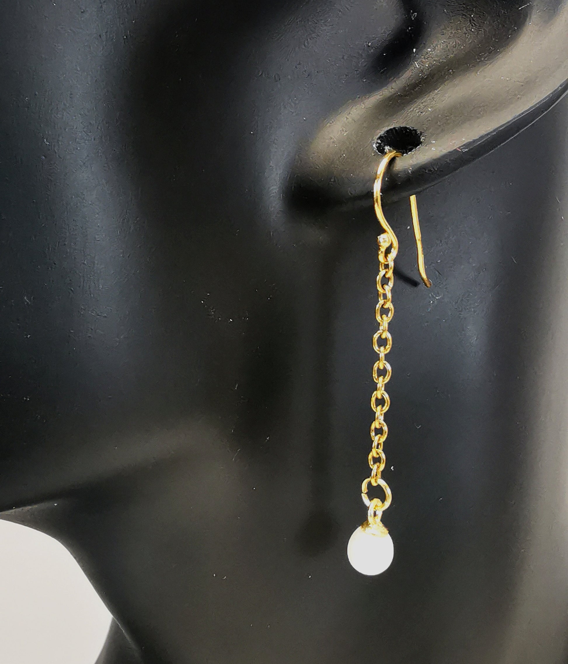 Boucles d'oreilles perles de culture blanches rondes 5mm sur pendants et chaînes plaqués or. Représentées par une boucle accrochée à une oreille de mannequin buste noir. Vue en gros plan de coté.