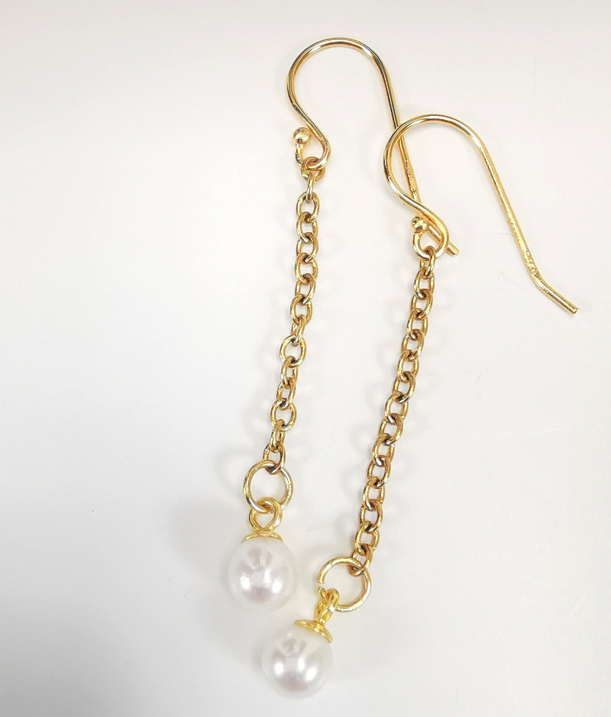 Boucles d'oreilles perles de culture blanches rondes 5mm sur pendants et chaînes plaqués or. Présentées cote à cote, boucle de gauche décalée vers le haut, sur fond blanc. Vue de dessus.