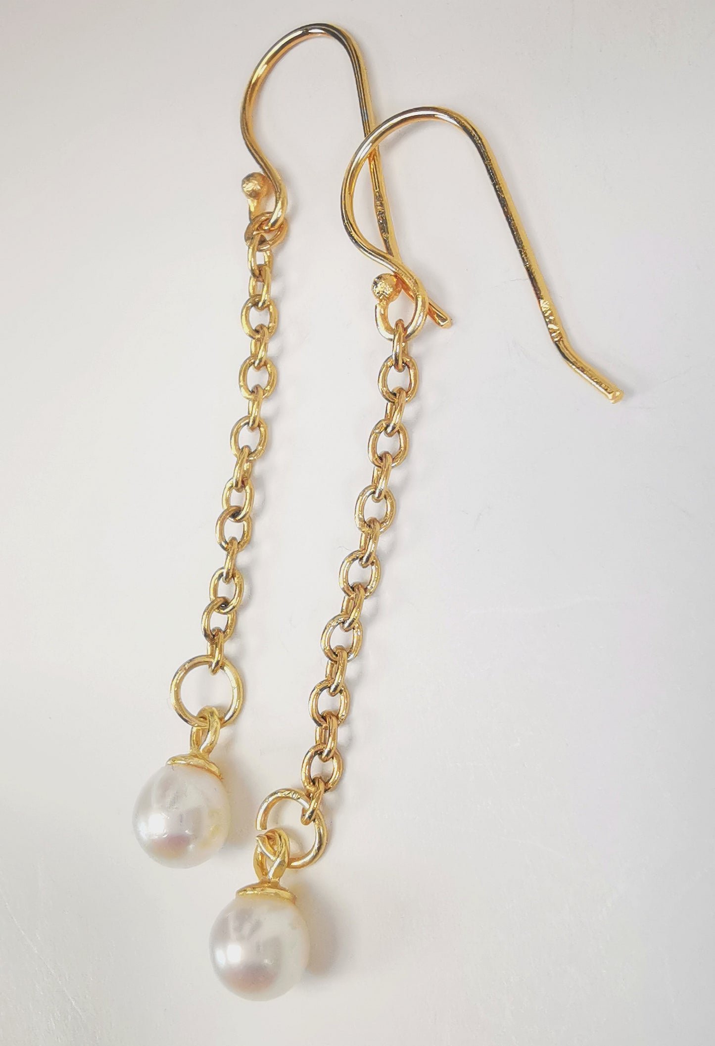 Boucles d'oreilles perles de culture blanches rondes 5mm sur pendants et chaînes plaqués or. Présentées cote à cote, boucle de gauche décalée vers le haut, sur fond blanc. Vue de la droite en gros plan.
