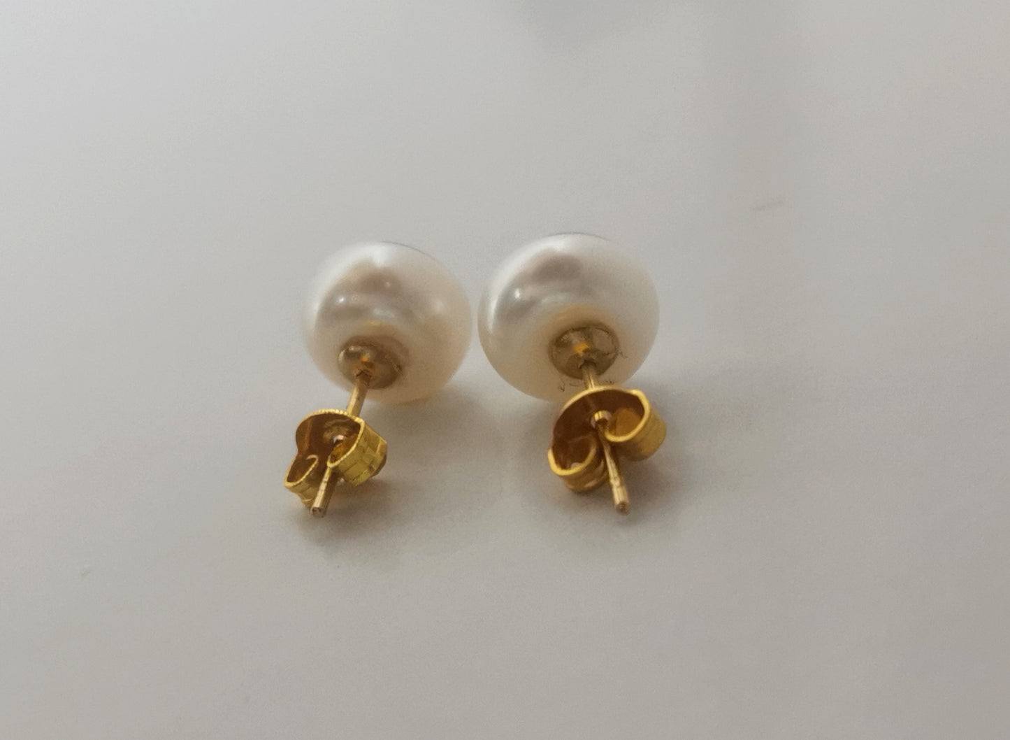 Boucles d'oreilles perles de culture blanches 9mm montées sur clous plaqués or. Présentées cote à cote, perles en haut, posées sur un fond blanc. Vue en très gros plan de face.