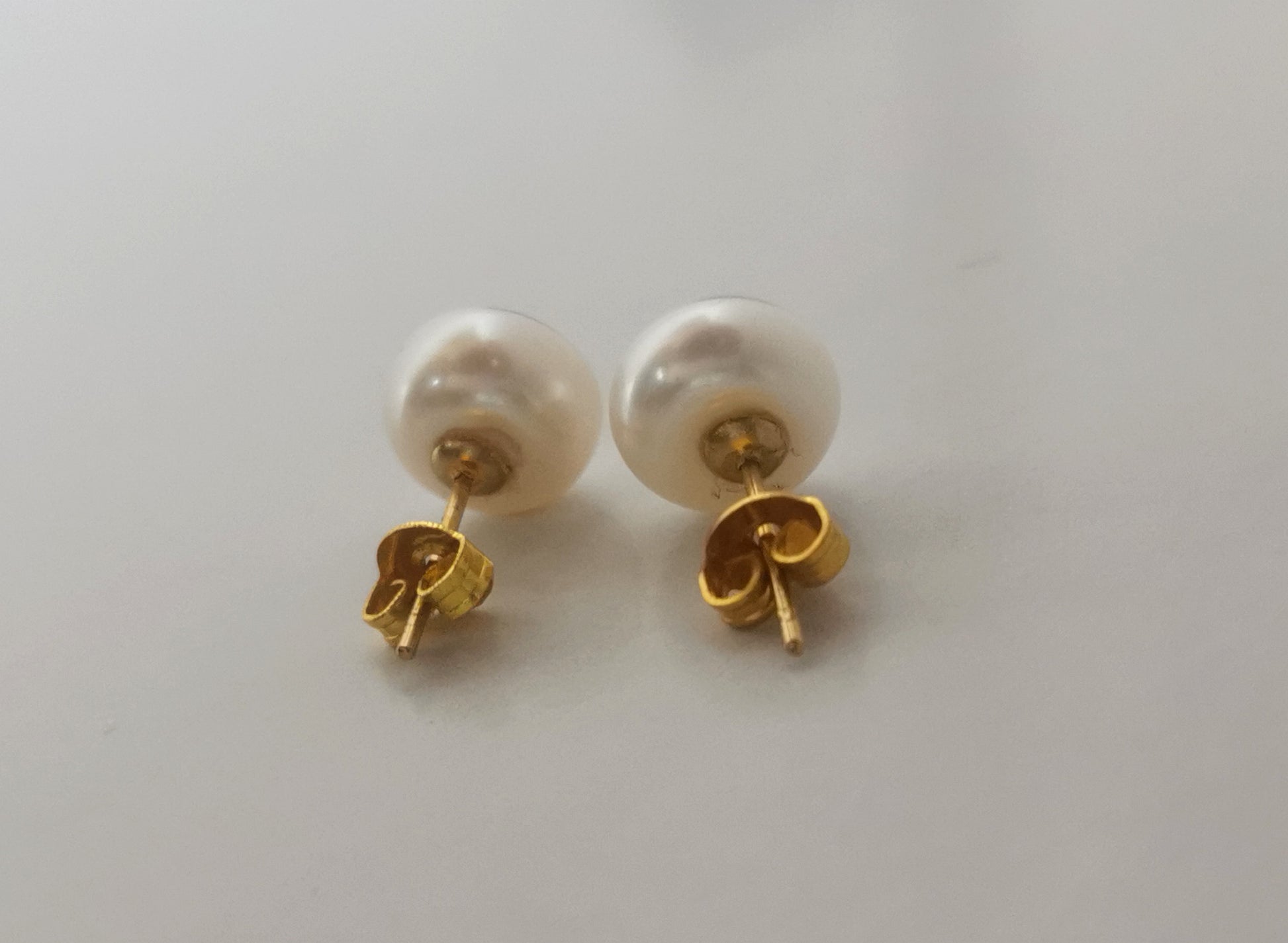 Boucles d'oreilles perles de culture blanches 9mm montées sur clous plaqués or. Présentées cote à cote, perles en haut, posées sur un fond blanc. Vue en très gros plan de face.