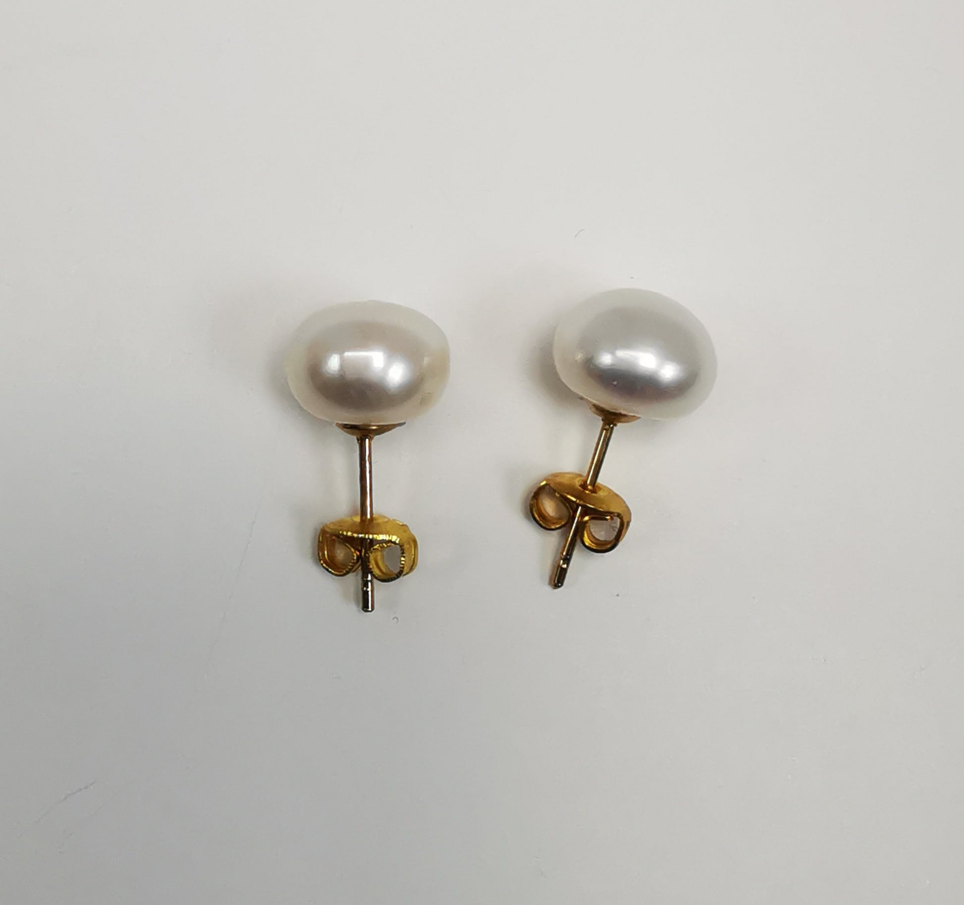 Boucles d'oreilles perles de culture blanches 9mm montées sur clous plaqués or. Présentées cote à cote, perles en haut, posées sur un fond blanc. Vue de dessus.