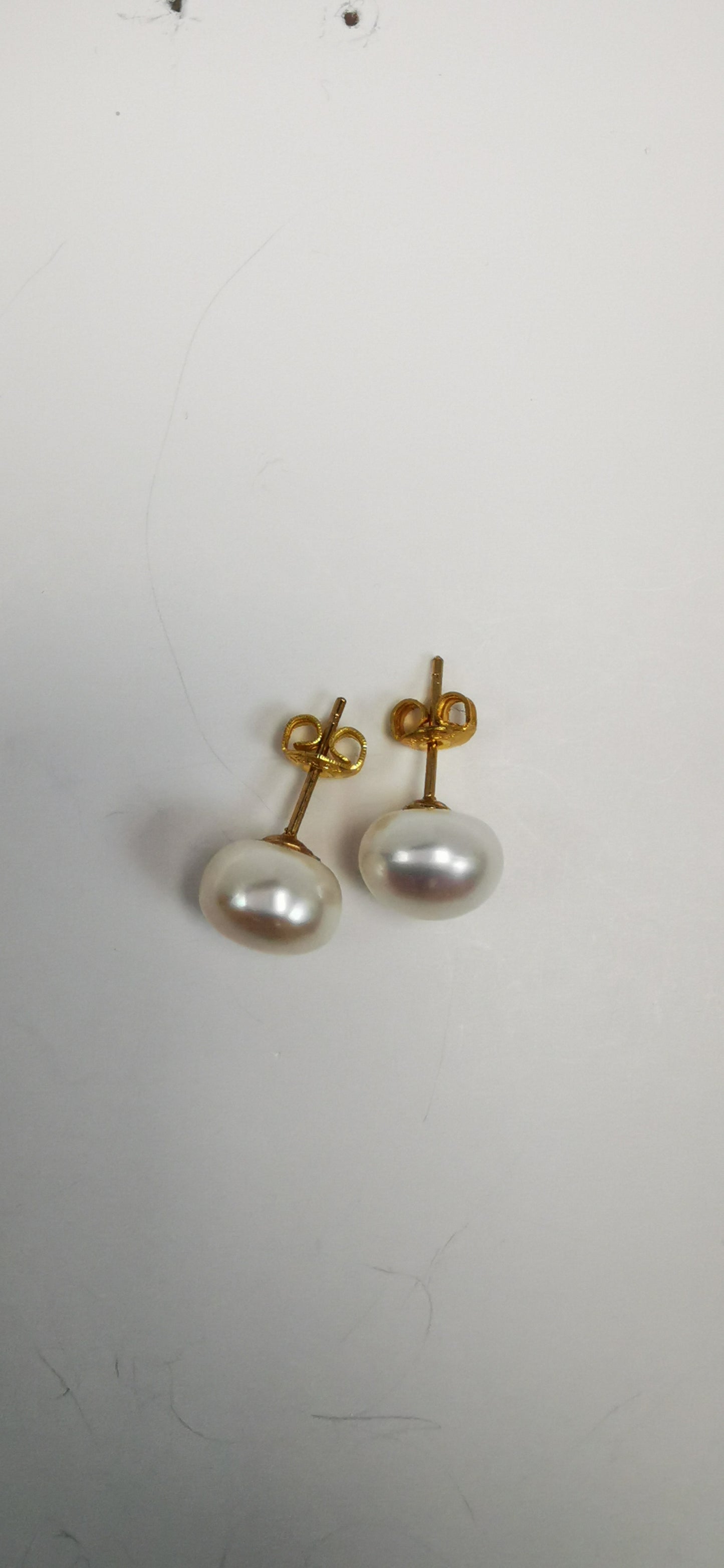 Boucles d'oreilles perles de culture blanches 9mm montées sur clous plaqués or. Présentées cote à cote, perles en bas, posées sur un fond blanc. Vue de dessus en plan large.