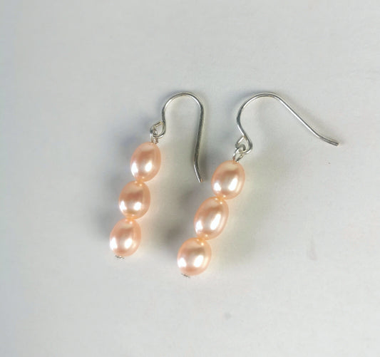 Boucles d'oreilles perles roses ,ovales 5-7mm, montées trois à la suite sur pendants argent, présentées posées sur un fond blanc, cote à cote. Vue de dessus .