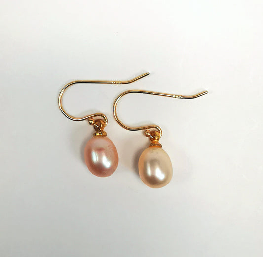 Boucles d'oreilles perles de culture ovales roses 7-9mm sur pendants plaqués or. Présentées cote à cote, perles en bas, pendants tournés vers la droite, sur fond blanc. Vue de dessus.