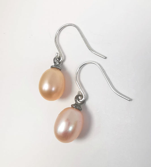 Boucles d'oreilles perles roses ,ovales 7-9mm, montées sur pendants argent, posées sur un fond blanc, cote à cote, la boucle gauche décalée vers le haut, pendants vers la droite. Vue de dessus .