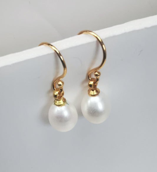 Boucles d'oreilles perles de culture blanches  7-9mm sur pendants plaquées or. Présentées suspendues à un support, cote à cote. Vue de trois quart gauche.