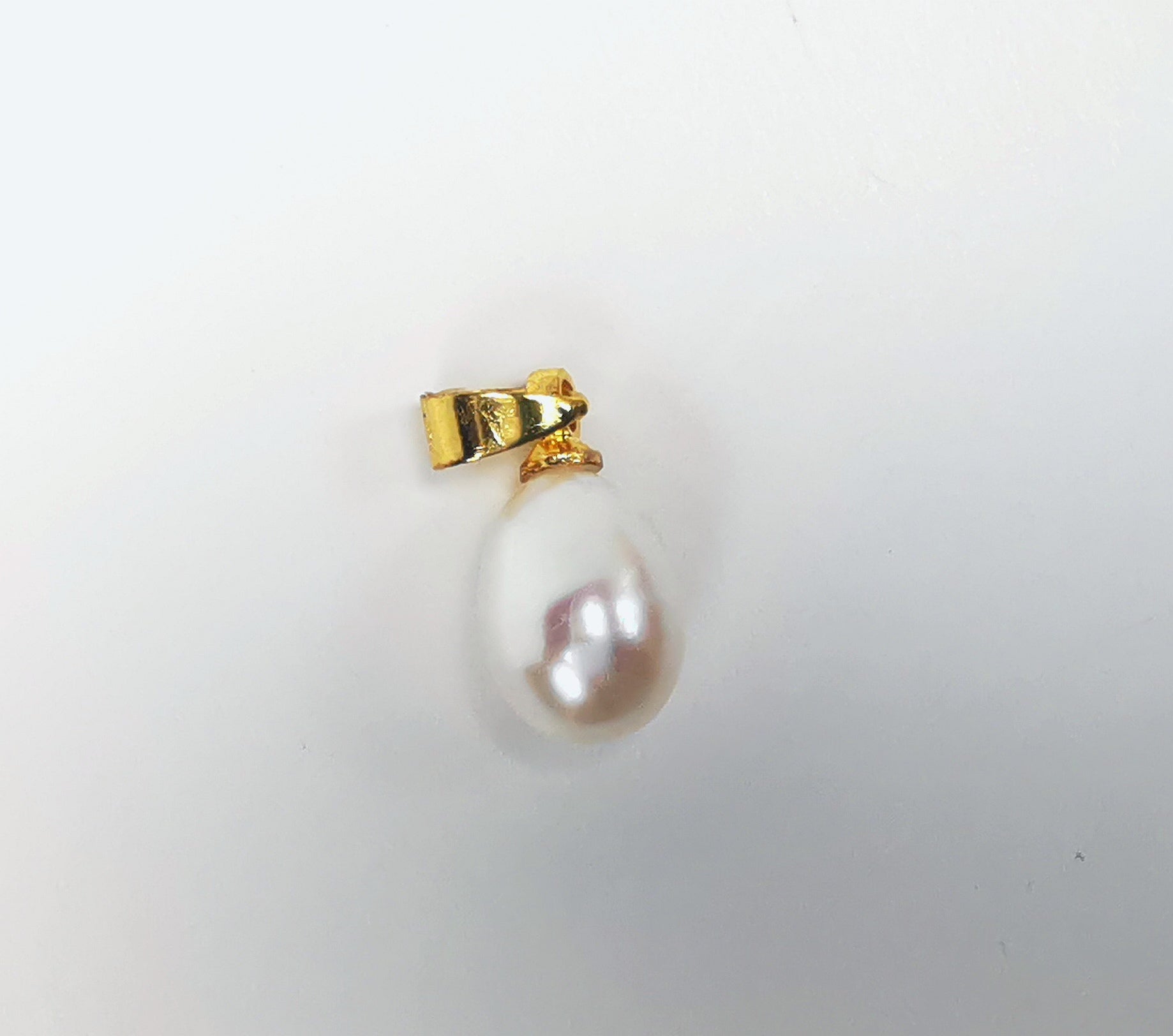 Boucles d'oreilles créoles plaquées or diamètre 50mm, fil 2mm sur lesquelles pendent des perles ovales blanches 7-9mm sur bélières plaquées or. Gros plan sur une perle et sa bélière sur fond blanc, vue de dessus.