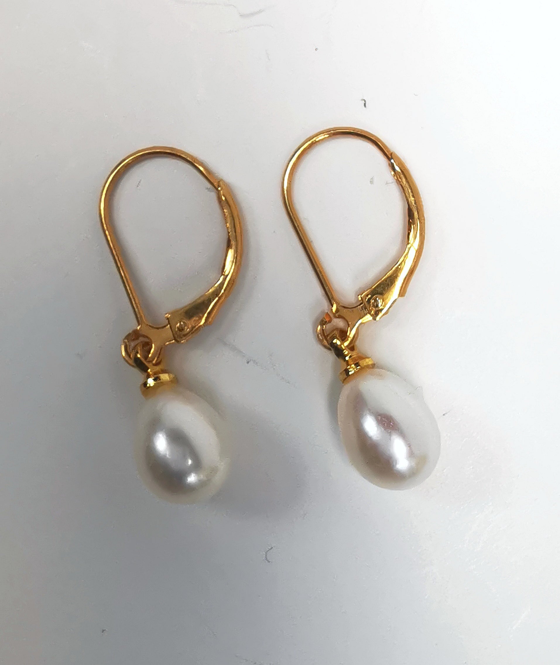 Boucles d'oreilles perles de culture blanches 7-9mm sur dormeuses plaquées or. Présentées posées sur un fond blanc, cote à cote, perles en bas. Vue de dessus.