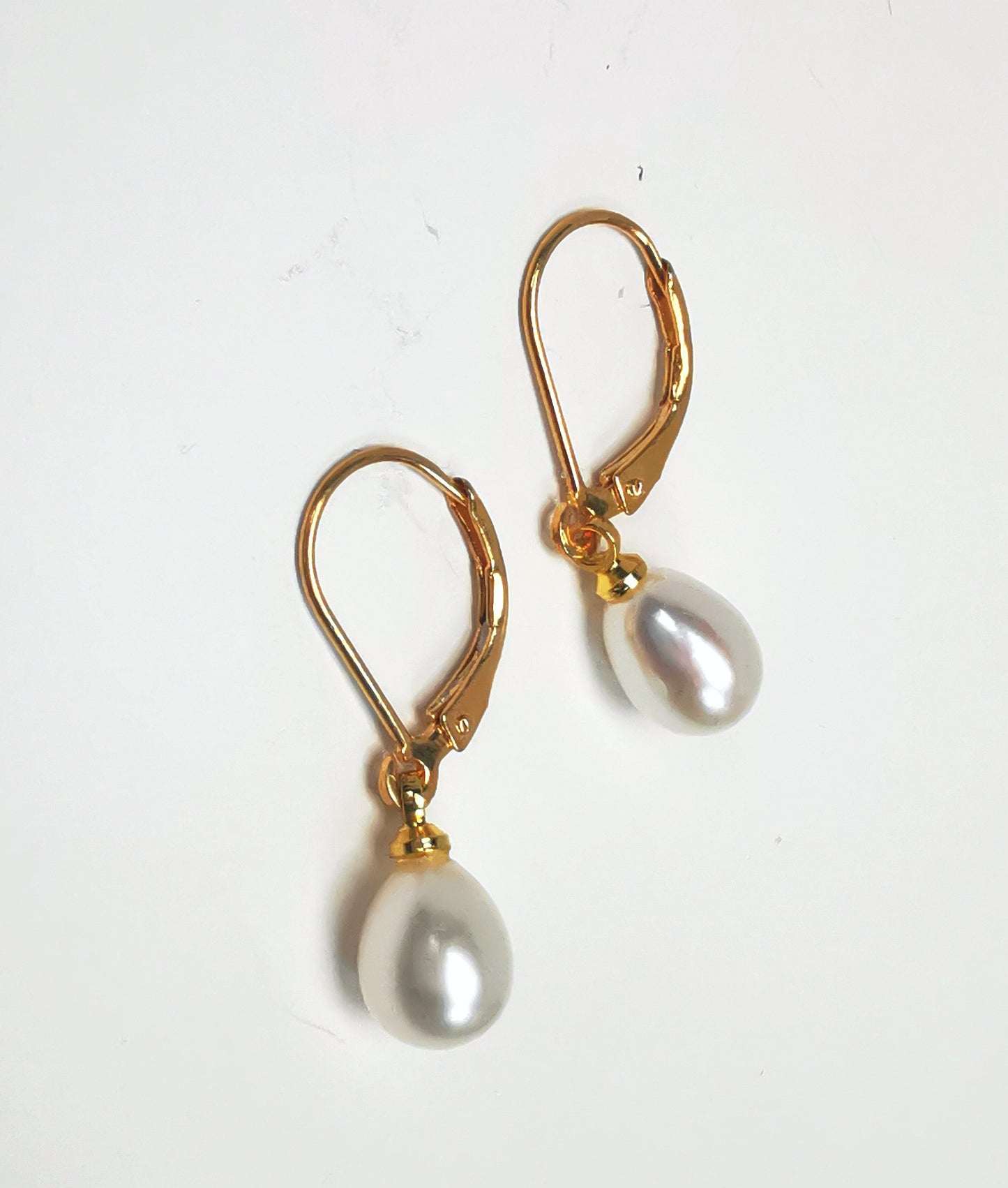 Boucles d'oreilles perles de culture blanches 7-9mm sur dormeuses plaquées or. Présentées posées sur un fond blanc, cote à cote, perles en bas celle de gauche décalée vers le bas. Vue de dessus.