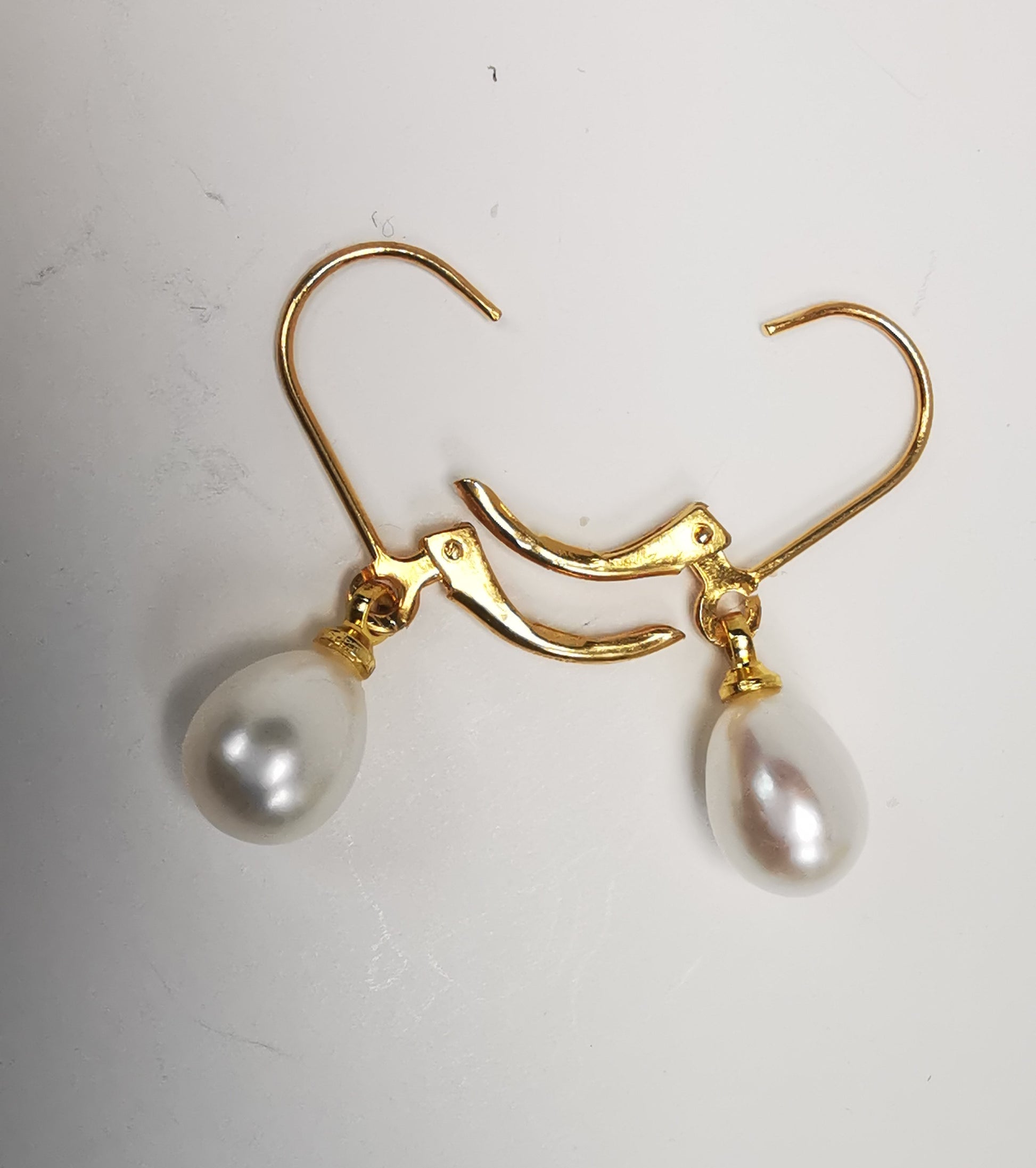Boucles d'oreilles perles de culture blanches 7-9mm sur dormeuses plaquées or. Présentées posées sur un fond blanc, cote à cote, perles en bas, dormeuses ouvertes. Vue de dessus.