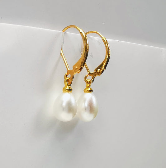 Boucles d'oreilles perles de culture blanches 7-9mm sur dormeuses plaquées or. Présentées suspendues à un support, cote à cote. Vue de trois quart gauche.