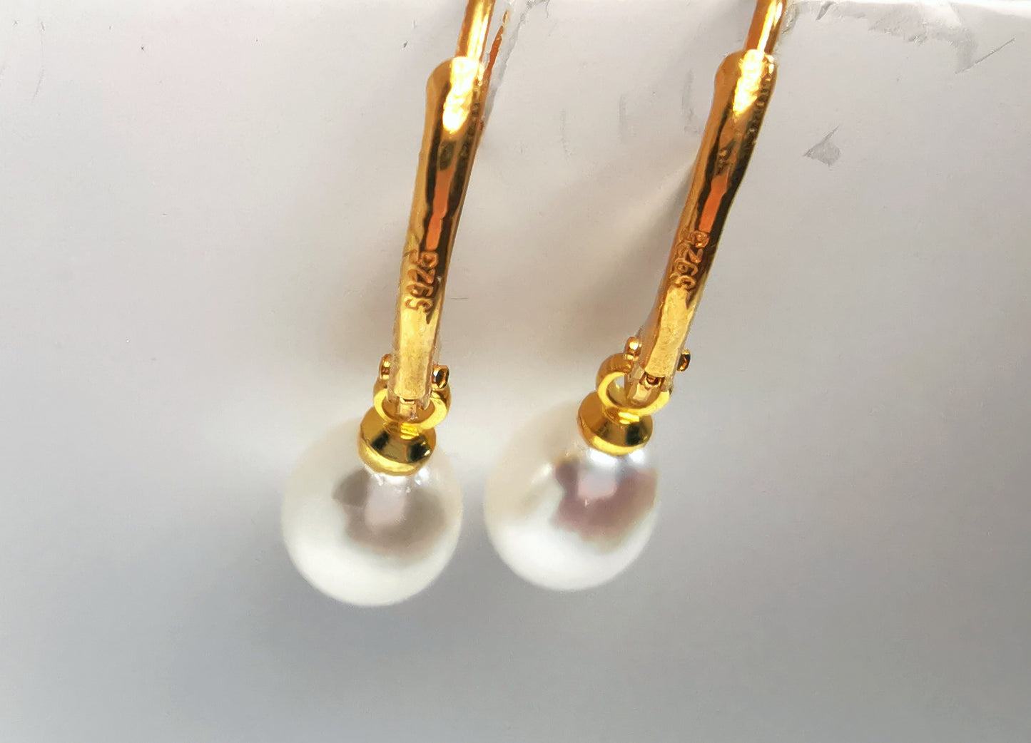 Boucles d'oreilles perles de culture blanches 7-9mm sur dormeuses plaquées or. Présentées suspendues à un support, cote à cote. Vue de dessus.