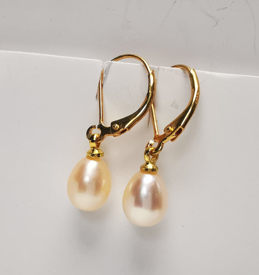 Boucles d'oreilles perles de culture roses 7-9mm sur dormeuses plaquées or. Présentées suspendues à un support, cote à cote. Vue de trois quart gauche.