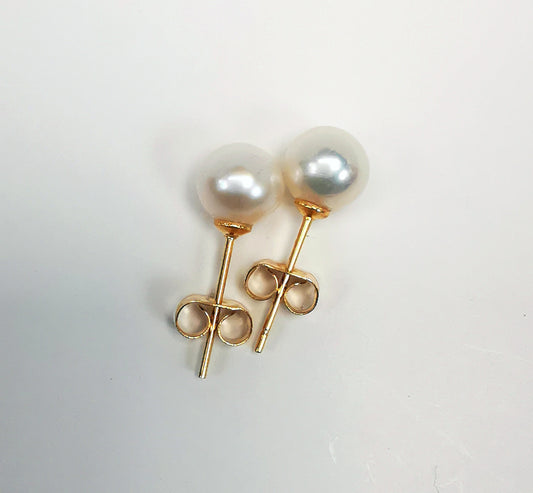 Boucles d'oreilles perles de culture blanches rondes sur clous plaqués or.Présentées cote à cote, perle en haut, la boucle de droite décalée vers le haut, sur fond blanc. Vue de dessus.