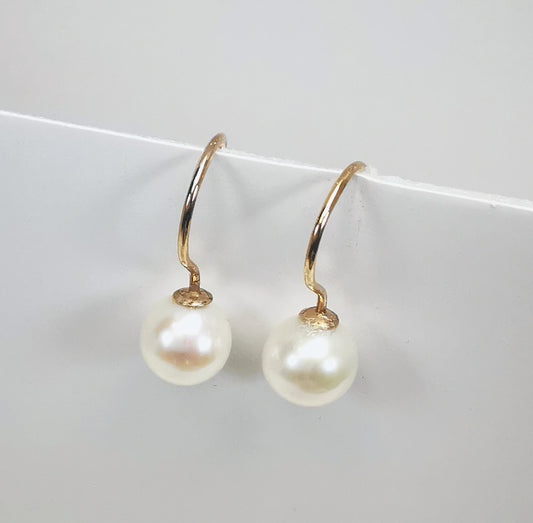 Boucles d'oreilles perles de culture blanches, rondes, 7mm sur pendants plaqués or. Présentées cote à cote, accrochées à un support sur fond blanc. Vue de droite en gros plan.