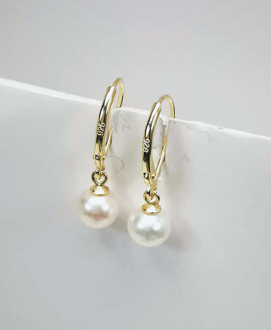 Boucles d'oreilles perles de culture blanches rondes 9mm sur dormeuses plaquées or. Présentées suspendues à un support, cote à cote. Vue de trois quart droit.