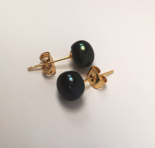 Boucles d'oreilles perles de culture noires 8mm sur clous plaqués or. Présentées à l'horizontale, l'une sur l'autre, boucle de dessus perles à droite décalée vers le haut, celle de dessous perle à gauche, sur fond blanc. Vue de face en gros plan.