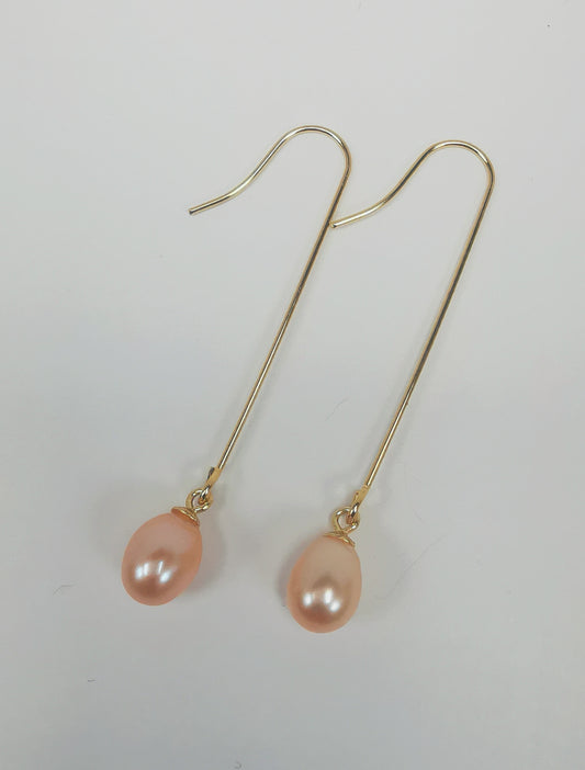 Boucles d'oreilles perles roses ,ovales 7-9mm, montées sur pendants or longs, 50mm, posées sur un fond blanc, cote à cote, les pendants inclinés vers la gauche, sur fond blanc.. Vue de dessus.
