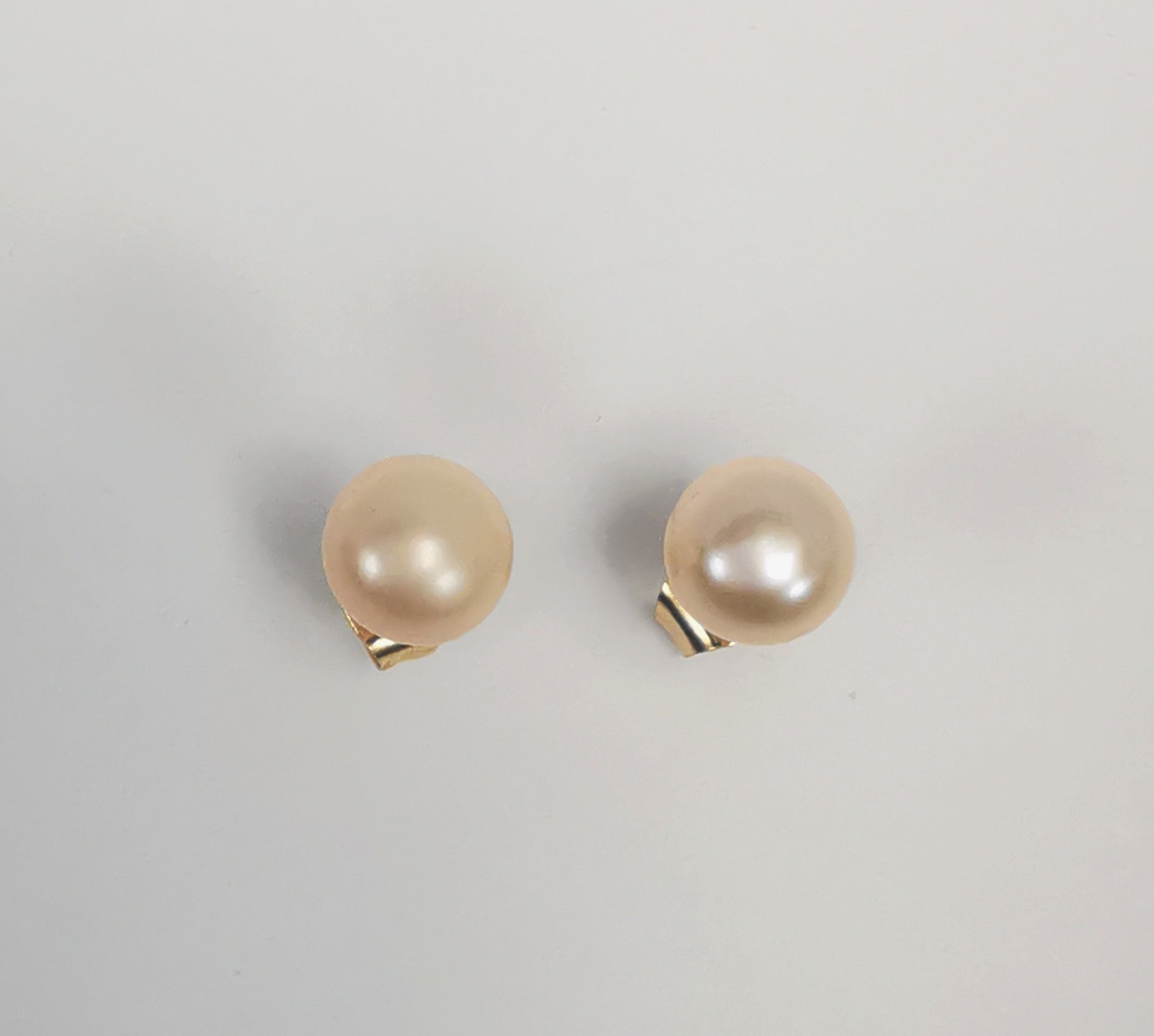 Boucles d'oreilles perles de culture rose 7mm sur clous plaqués or. Présentées l'une au dessus de l'autre plantées sur un fond blanc. Vue de dessus.
