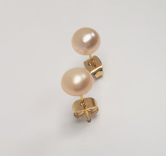 Boucles d'oreilles perles de culture rose 7mm sur clous plaqués or. Présentées l'une au dessus de l'autre plantées sur un fond blanc, inclinées vers l'arrière. Vue de face.