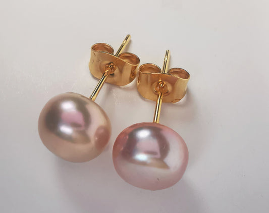 Boucles d'oreilles perles de culture parme 8mm, sur clous plaqués or. Présentées cote à cote, perles en bas, sur fond blanc. Vue de dessus en gros plan.