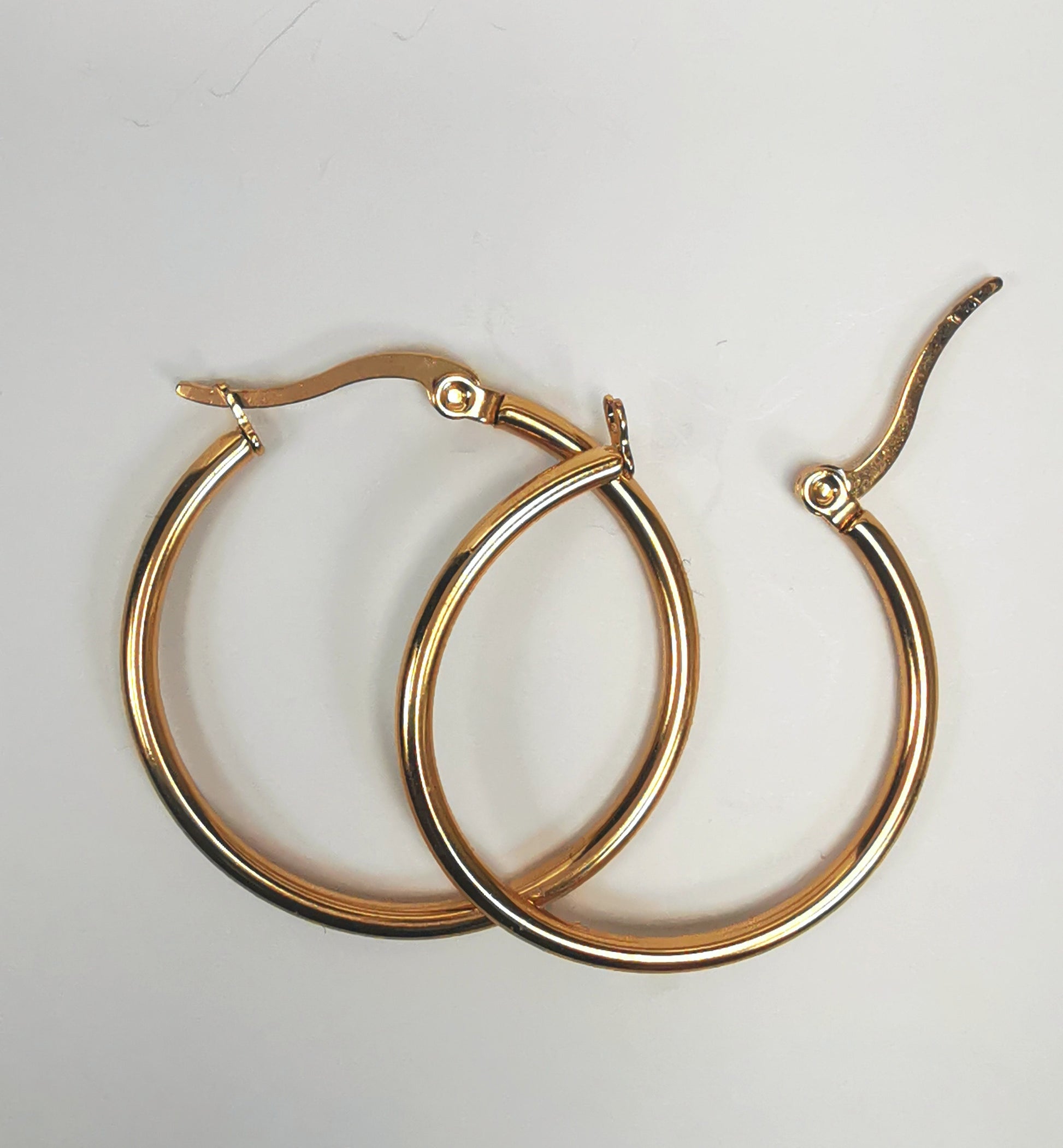 Boucles d'oreilles créoles inox plaqué or, diamètre 30mm, fil de 2mm. Présentées posées sur fond blanc, l'une sur l'autre, celle de droite fermoir ouvert. Vue de dessus.