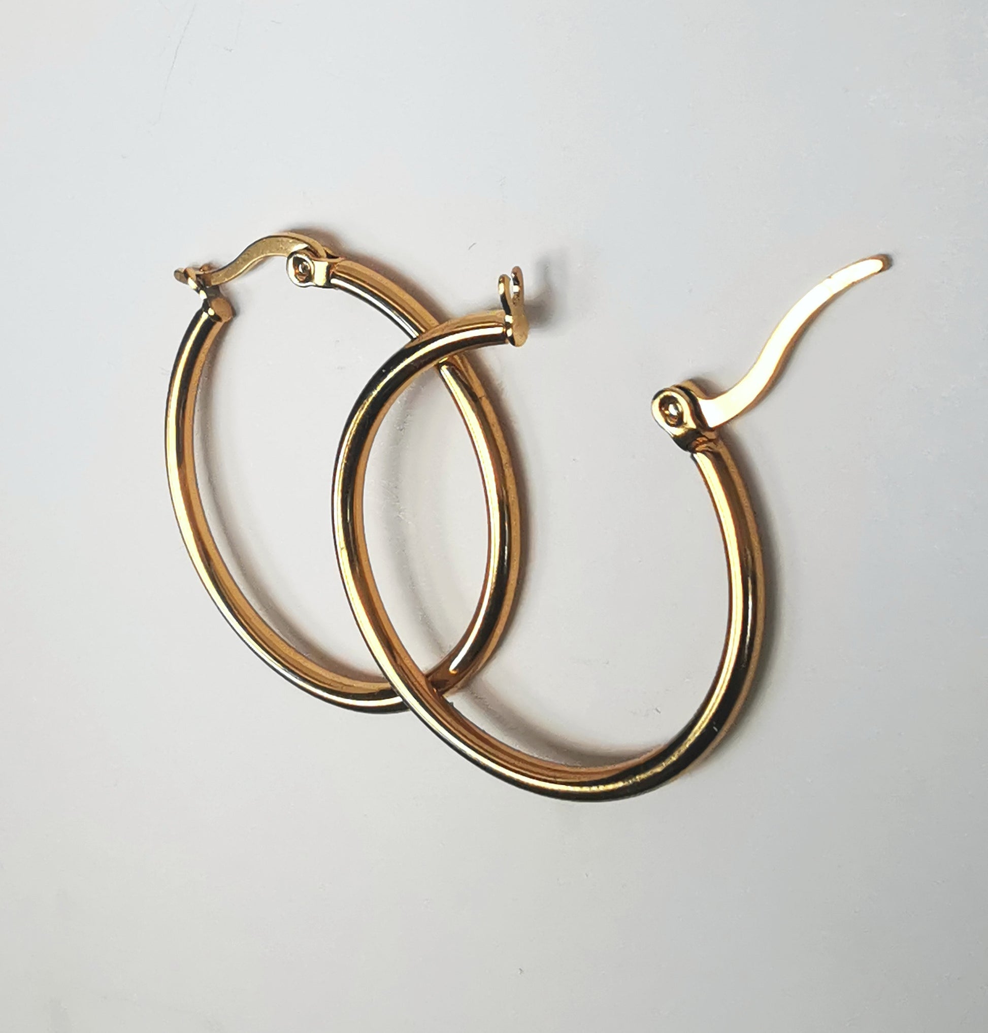 Boucles d'oreilles créoles inox plaqué or, diamètre 30mm, fil de 2mm. Présentées posées sur fond blanc, l'une sur l'autre, celle de droite fermoir ouvert. Vue depuis la droite.