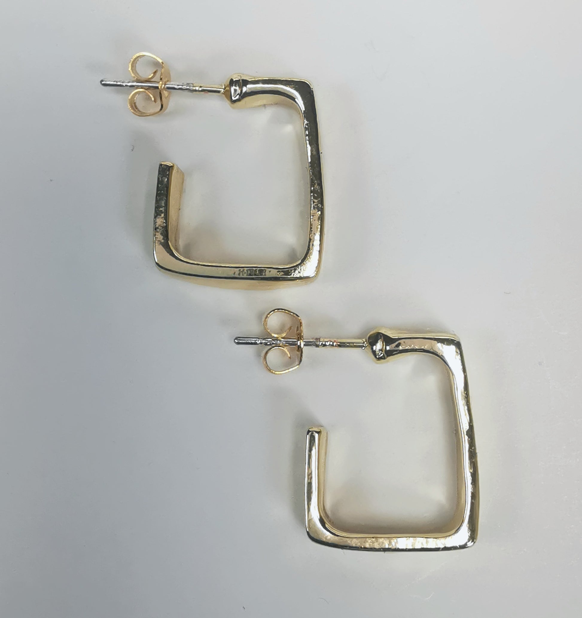 Boucles d'oreilles dorées, carrées, de 15mm de coté ,avec section rectangulaire, présentées posées sur fond blanc, cote à cote, la boucle droite décalée vers le bas. Vue de dessus.