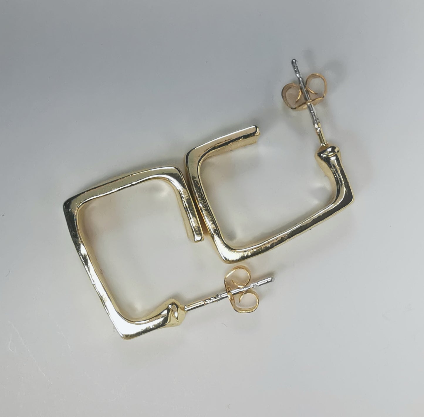 Boucles d'oreilles dorées, carrées, de 15mm de coté ,avec section rectangulaire, présentées posées sur fond blanc, cote à cote, la boucle droite décalée de 90 degrés. Vue de dessus.