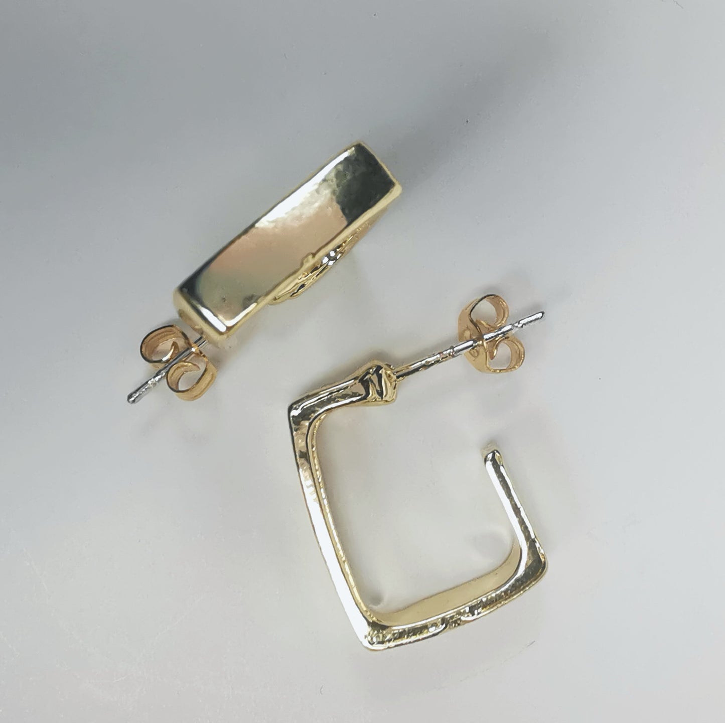 Boucles d'oreilles dorées, carrées, de 15mm de coté ,avec section rectangulaire, présentées posées sur fond blanc, l'une à plat, l'autre sur champ Vue de dessus.
