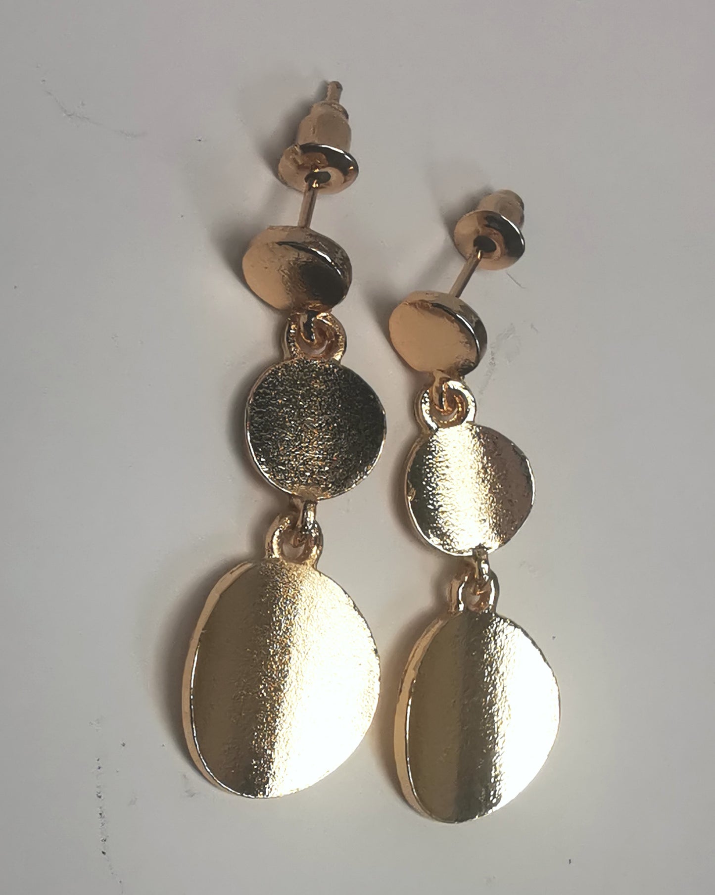 Boucles d'oreilles pendantes sur clous en métal doré texturé. Un disque de10mm sur clou en dessous un autre de 12mm et un troisième de 16mm. Présentées par paire, cote à cote, posées sur fond blanc. Vue de dessus.
