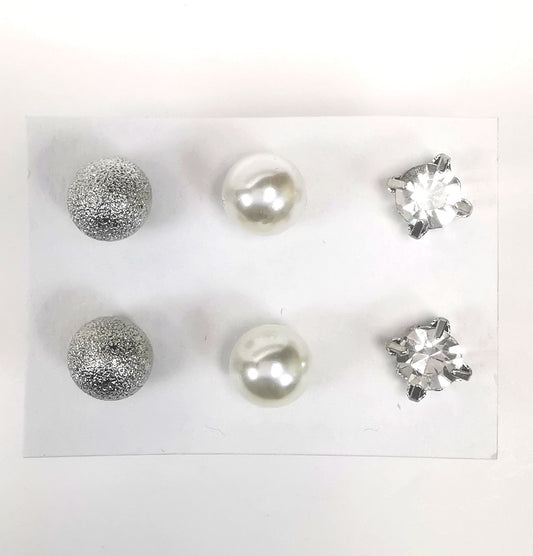 Trios de boucles d'oreilles puces fantaisie, la première est une sphère texturée argentée, la deuxième une perle fantaisie blanche et la troisième un faux diamant en strass de 6mm de coté. Présentées  plantées sur un fond blanc, vue de dessus.