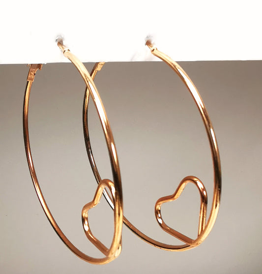 Boucles d'oreilles créoles  dorées 53mm, fil de 2mm, et coeur formé en bas avec le fil. Présentées  accrochées sous un support, l'une à coté de l'autre. Vue légèrement de gauche.