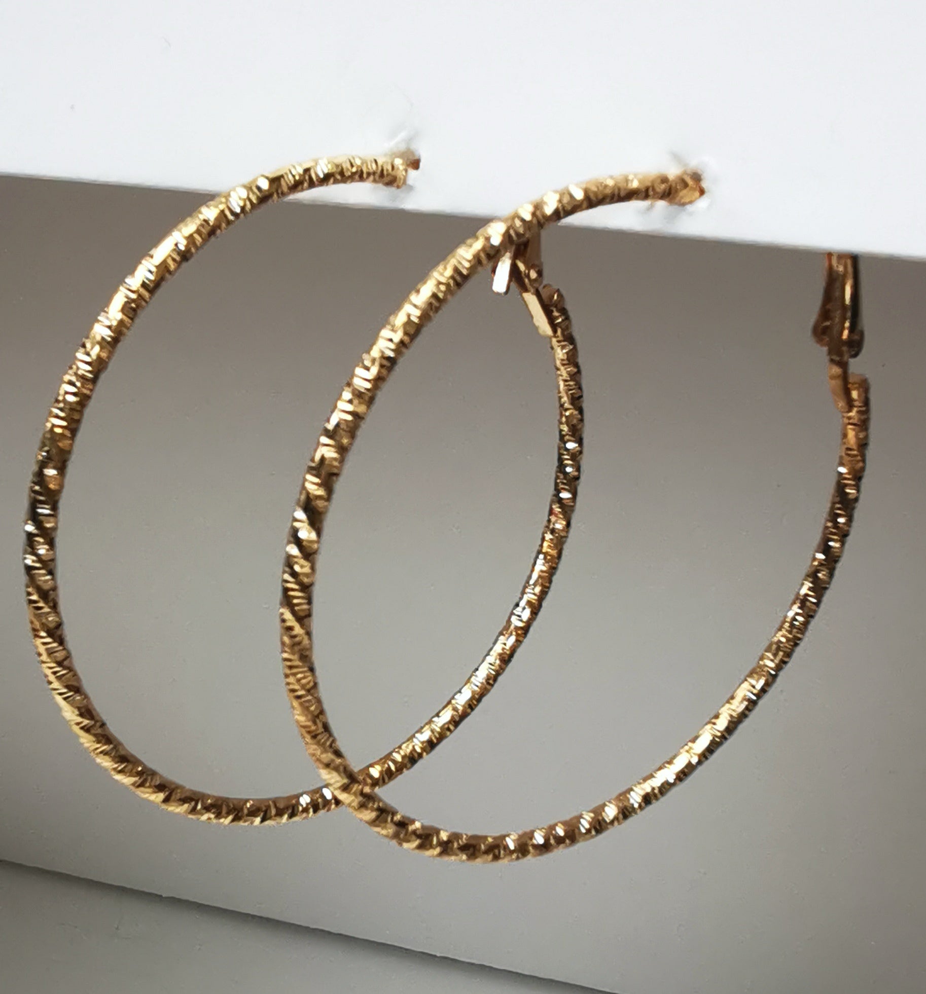 Boucles d'oreilles créoles dorées 50mm de diamètre, fil de 1.5mm, surface texturée. Accrochées sous un support, vue de droite en gros plan.