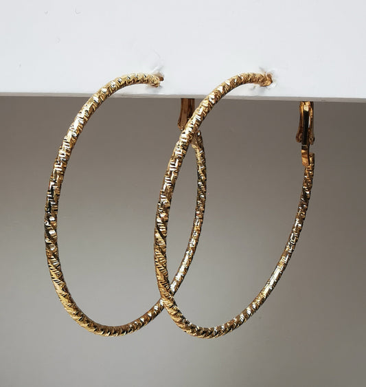 Boucles d'oreilles créoles dorées 50mm de diamètre, fil de 1.5mm, surface texturée. Accrochées sous un support, vue de droite