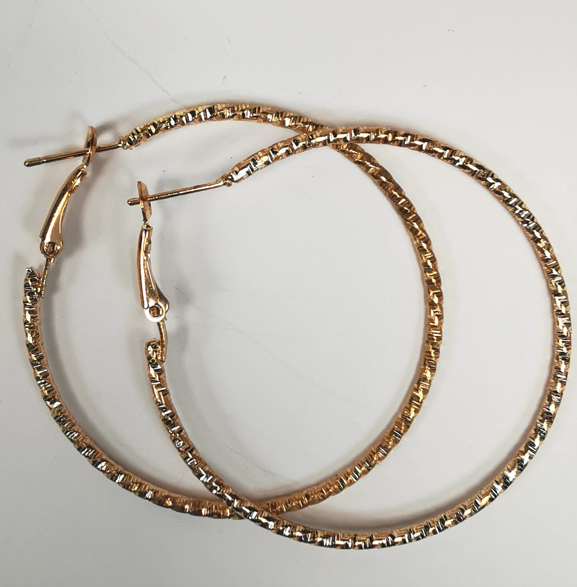 Boucles d'oreilles créoles dorées 50mm de diamètre, fil de 1.5mm, surface texturée. Posées l'une sur l'autre sur un fond blanc, vue de dessus.