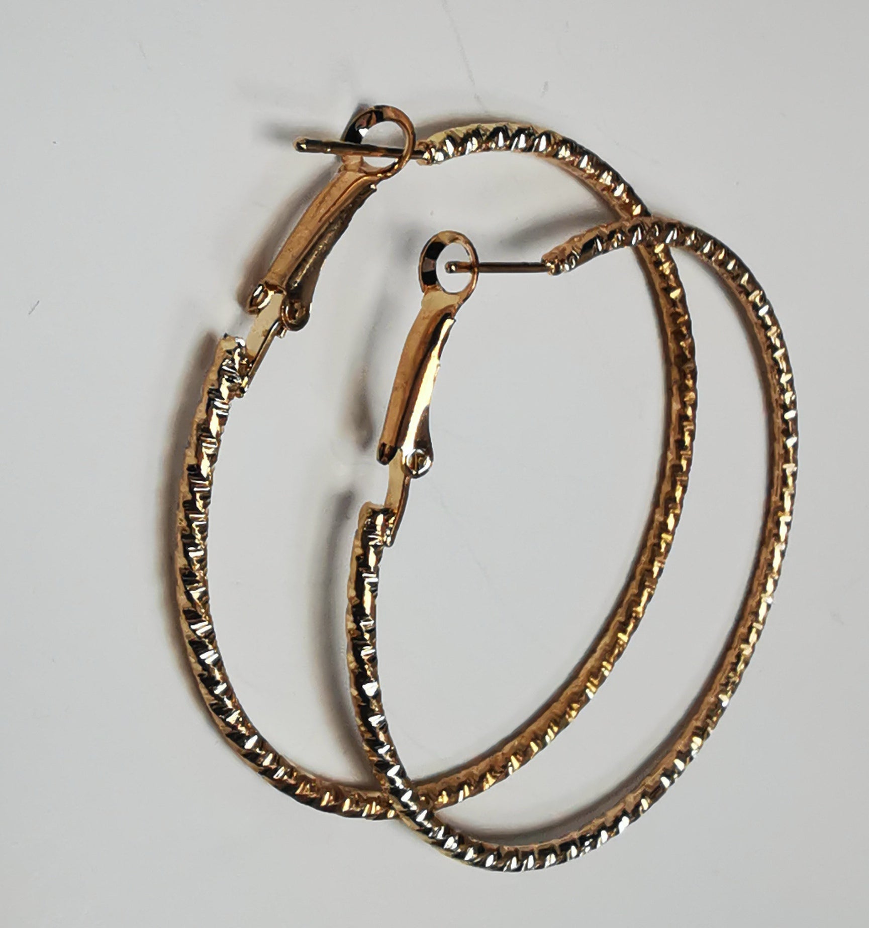 Boucles d'oreilles créoles dorées 50mm de diamètre, fil de 1.5mm, surface texturée. Posées sur fond blanc l'une sur l'autre, vue de gauche.