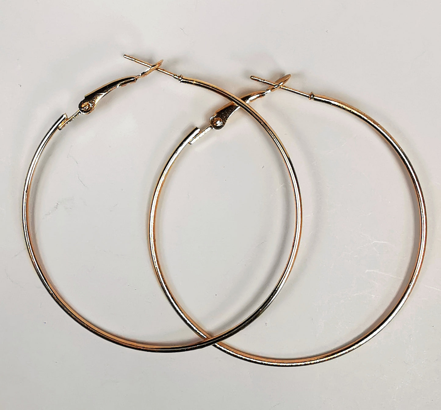 Boucles d'oreilles créoles dorées diamètre 50mm, fil 1mm, posées l'une sur l'autre sur fond blanc,. vue de dessus.