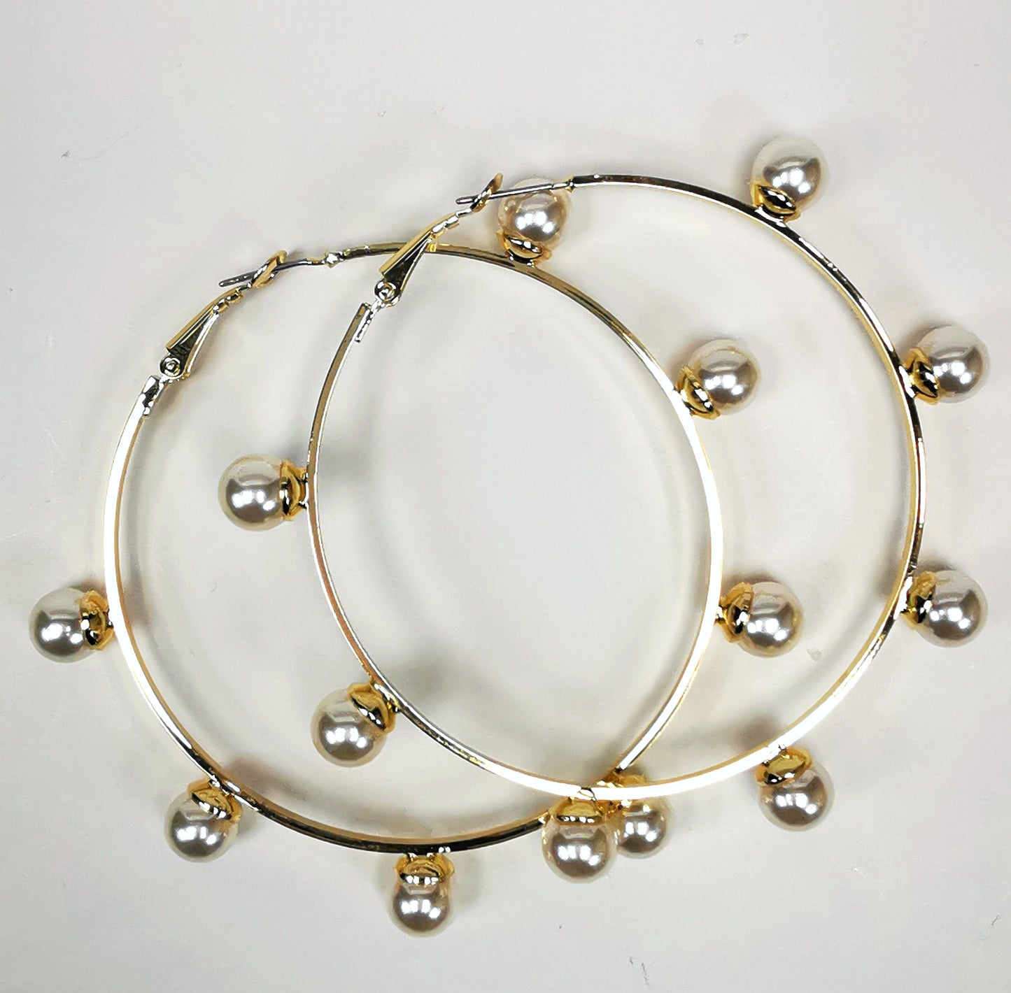 Boucles d'oreilles créoles dorées, diamètre 63mm avec 6 perles fantaisie de 8mm sur l'extérieur. présentées posées sur un fond blanc, l'une sur l'autre. Vue de dessus.