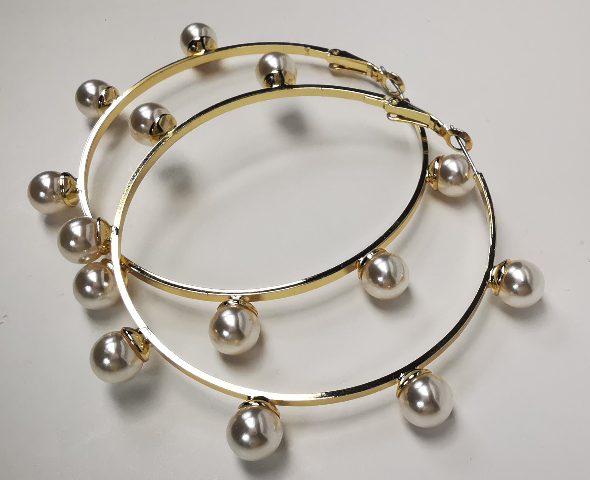 Boucles d'oreilles créoles dorées, diamètre 63mm avec 6 perles fantaisie de 8mm sur l'extérieur. présentées posées sur un fond blanc, l'une sur l'autre. Vue de coté