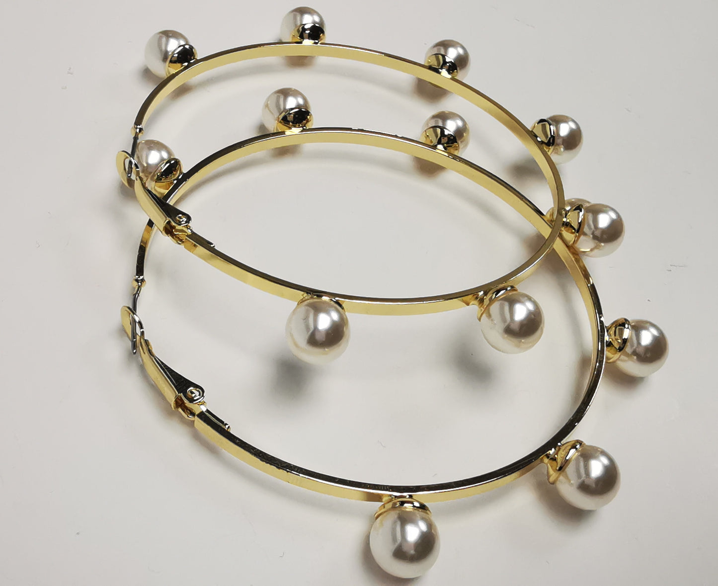 Boucles d'oreilles créoles dorées, diamètre 63mm avec 6 perles fantaisie de 8mm sur l'extérieur. présentées posées sur un fond blanc, l'une sur l'autre. Vue de gauche.
